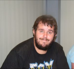 Mann mit dunklem Bart und schwarzem T-Shirt vor heller Wand, Transport und Logistik Saalfelden